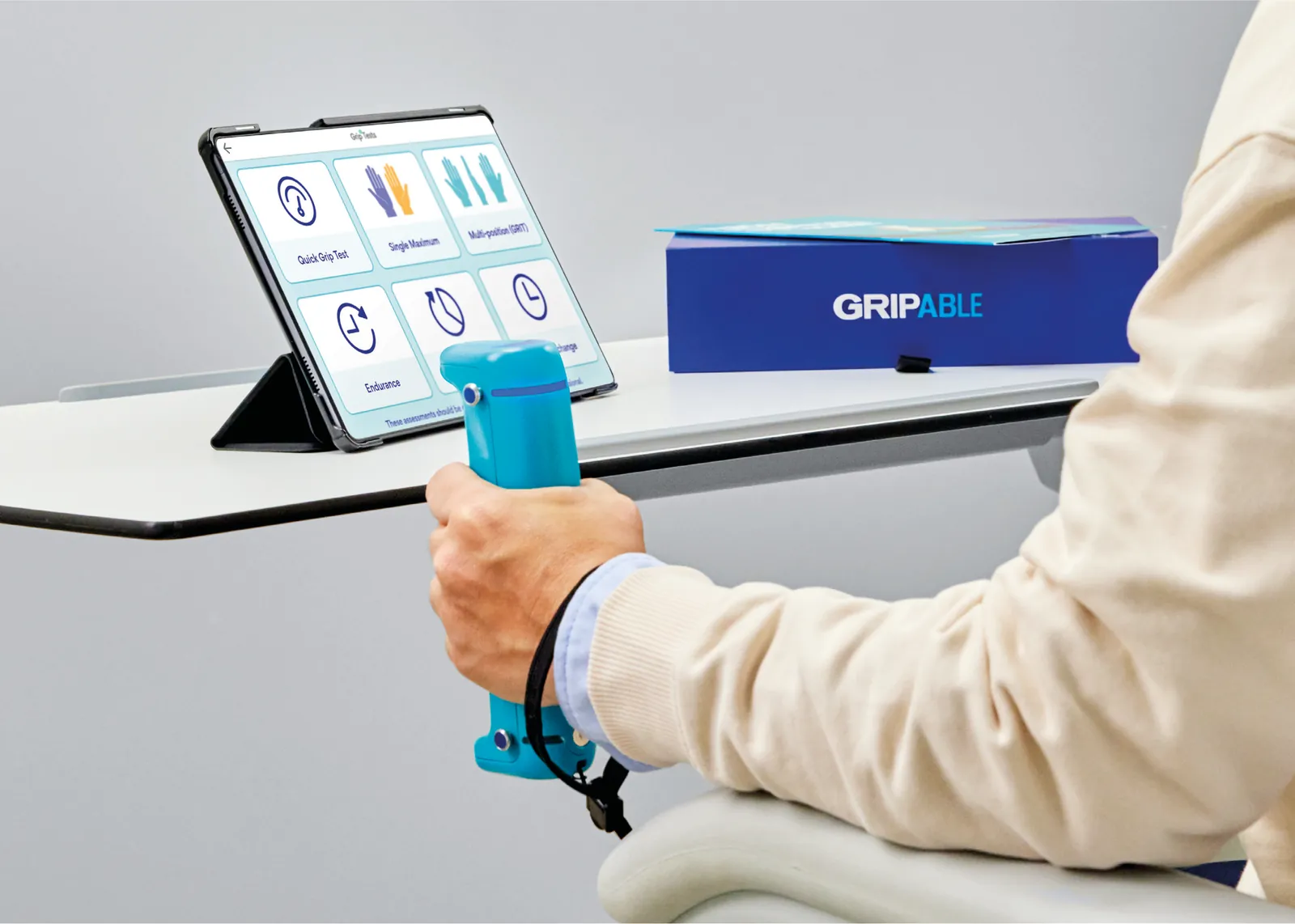 Paziente che esegue un test di presa con GripAble davanti al tablet con il menu dei test